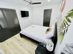 A bedroom with a bed, a ceiling fan, a TV, and a door.