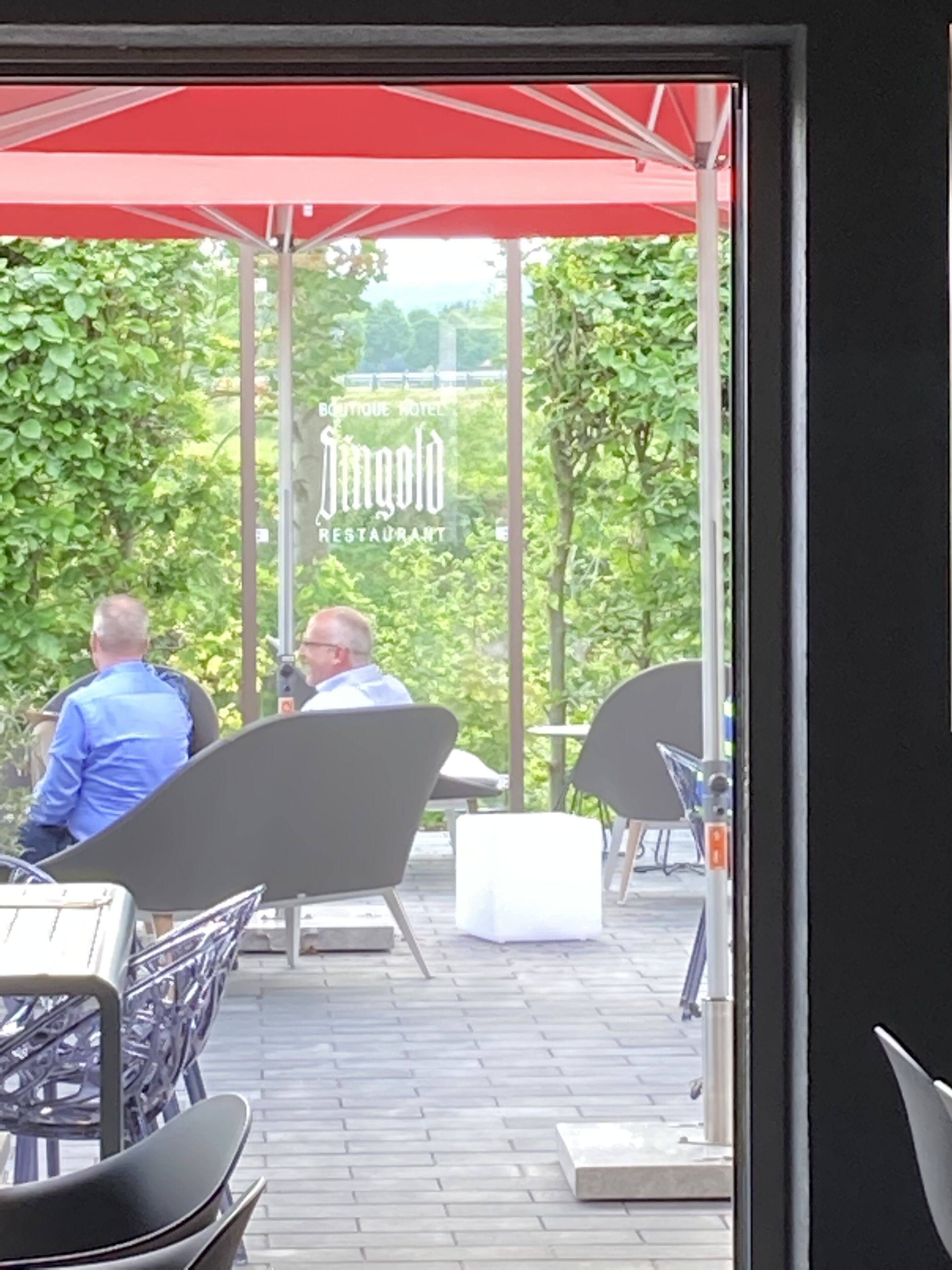 Ein Außenbereich mit Tischen und Stühlen, einem roten Sonnenschirm und einem Schild für ein Restaurant.