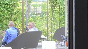 Ein Außenbereich mit Tischen und Stühlen, einem roten Sonnenschirm und einem Schild für ein Restaurant.
