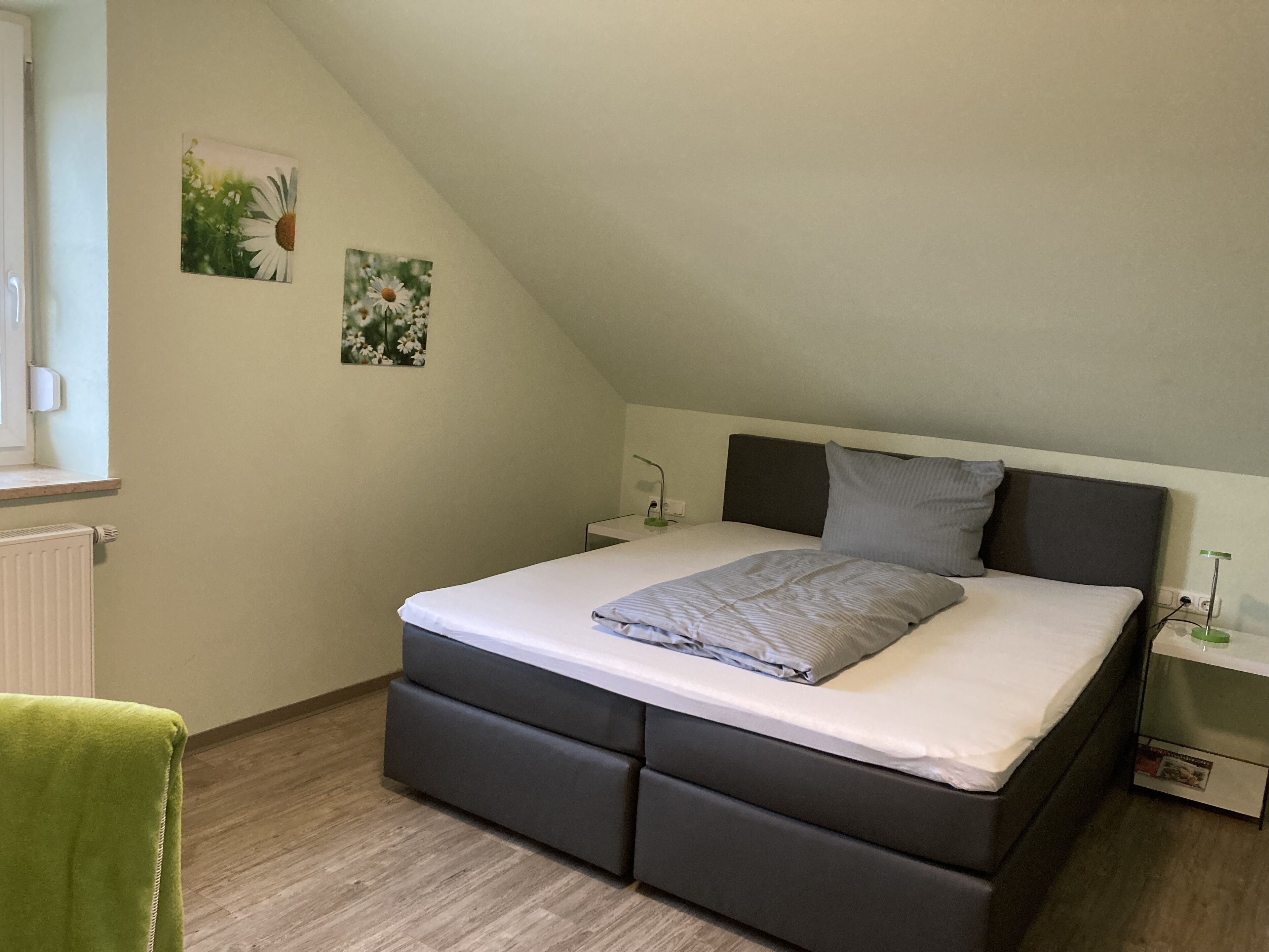 A bedroom with a bed, a nightstand, a lamp, and a radiator.
