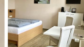 Camera d'albergo moderna con un letto di legno, una scrivania bianca, una poltrona in vimini, un televisore a schermo piatto e un armadio.