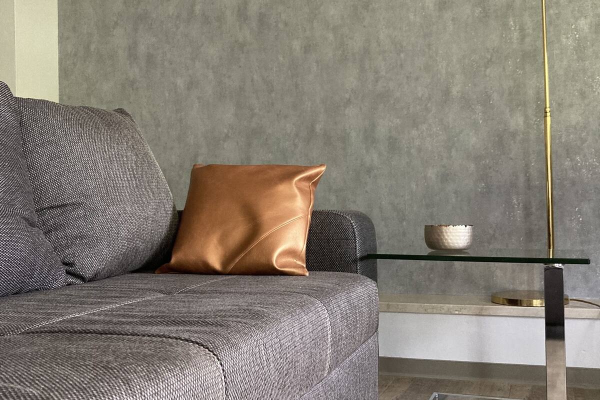 A modern living room with a grey sofa, a brown accent pillow, a glass coffee table, and a gold floor lamp.