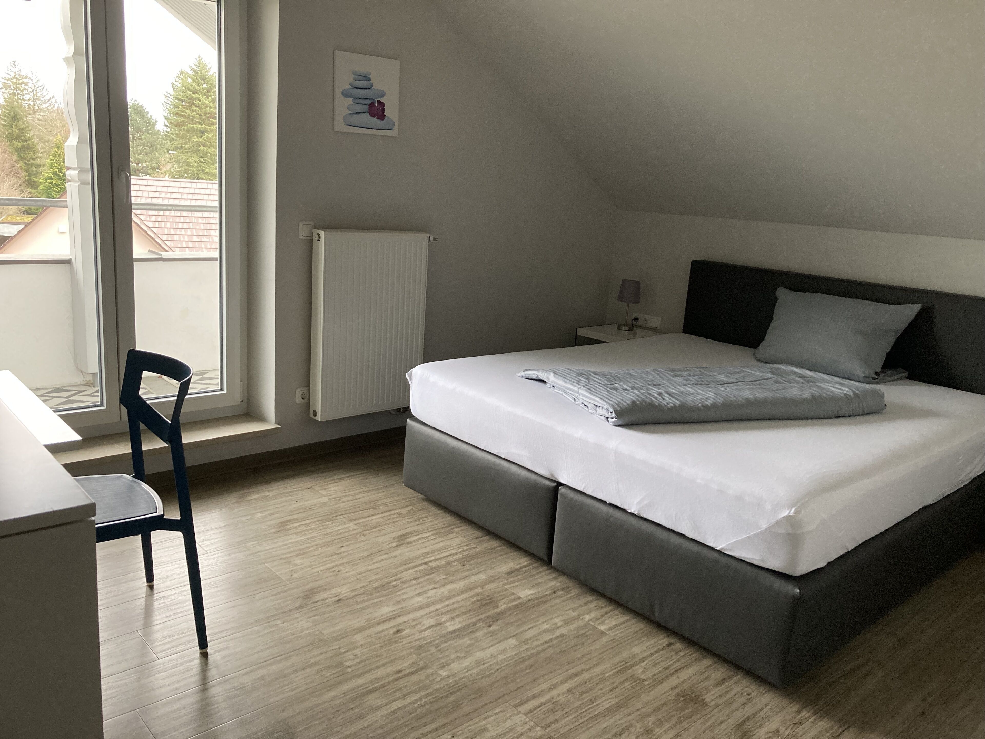 Ein Schlafzimmer mit Bett, Sessel, Nachttisch, Heizkörper und Fenster.