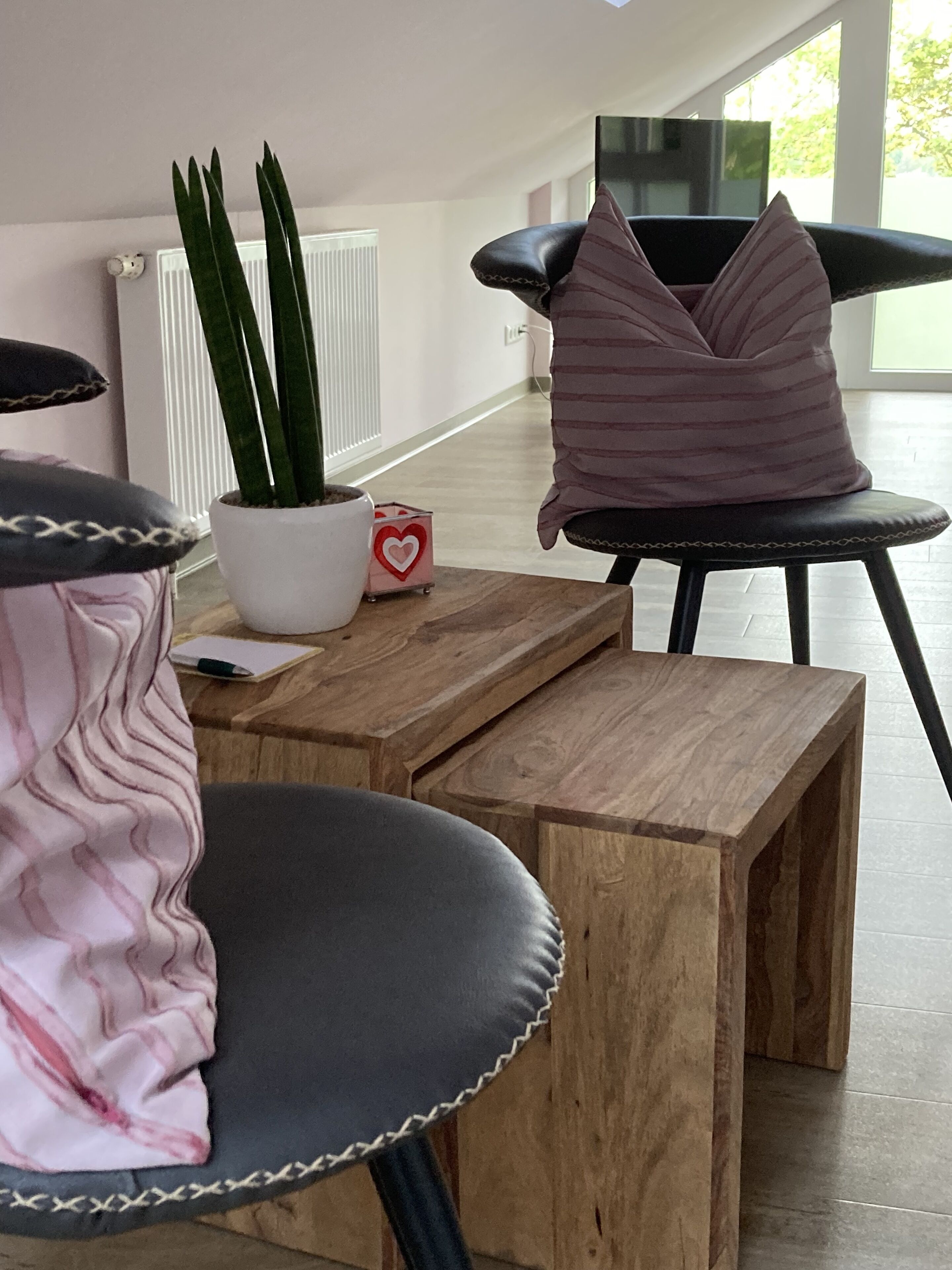 A modern room with a wooden table, a potted plant, and a chair with a cushion.