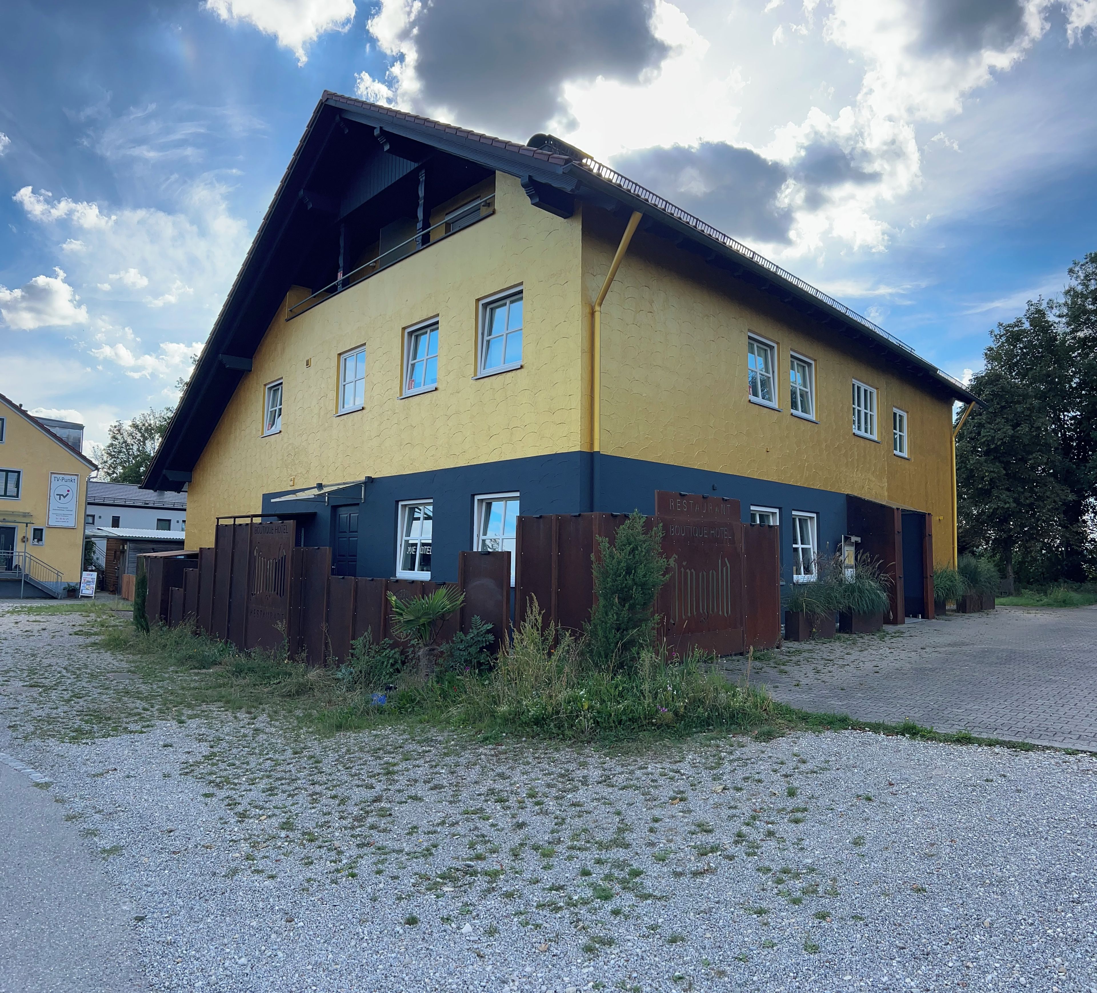 A two-story building with a flat roof, multiple windows, and a gravel driveway.