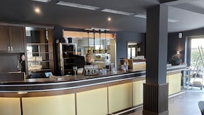 Un área de bar moderna con una barra curva, taburetes y un espacio de estar con mesas y sillas.