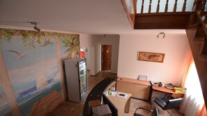 Una habitación con un escritorio curvo, un refrigerador, un mural en la pared y una escalera.