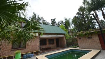 Une maison en briques avec un toit végétalisé, une piscine et de la verdure tout autour.