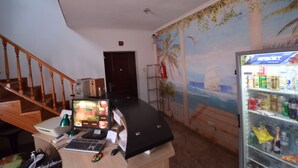 Una habitación con una escalera de madera, un ordenador de escritorio, un refrigerador lleno de bebidas y un mural con una playa.