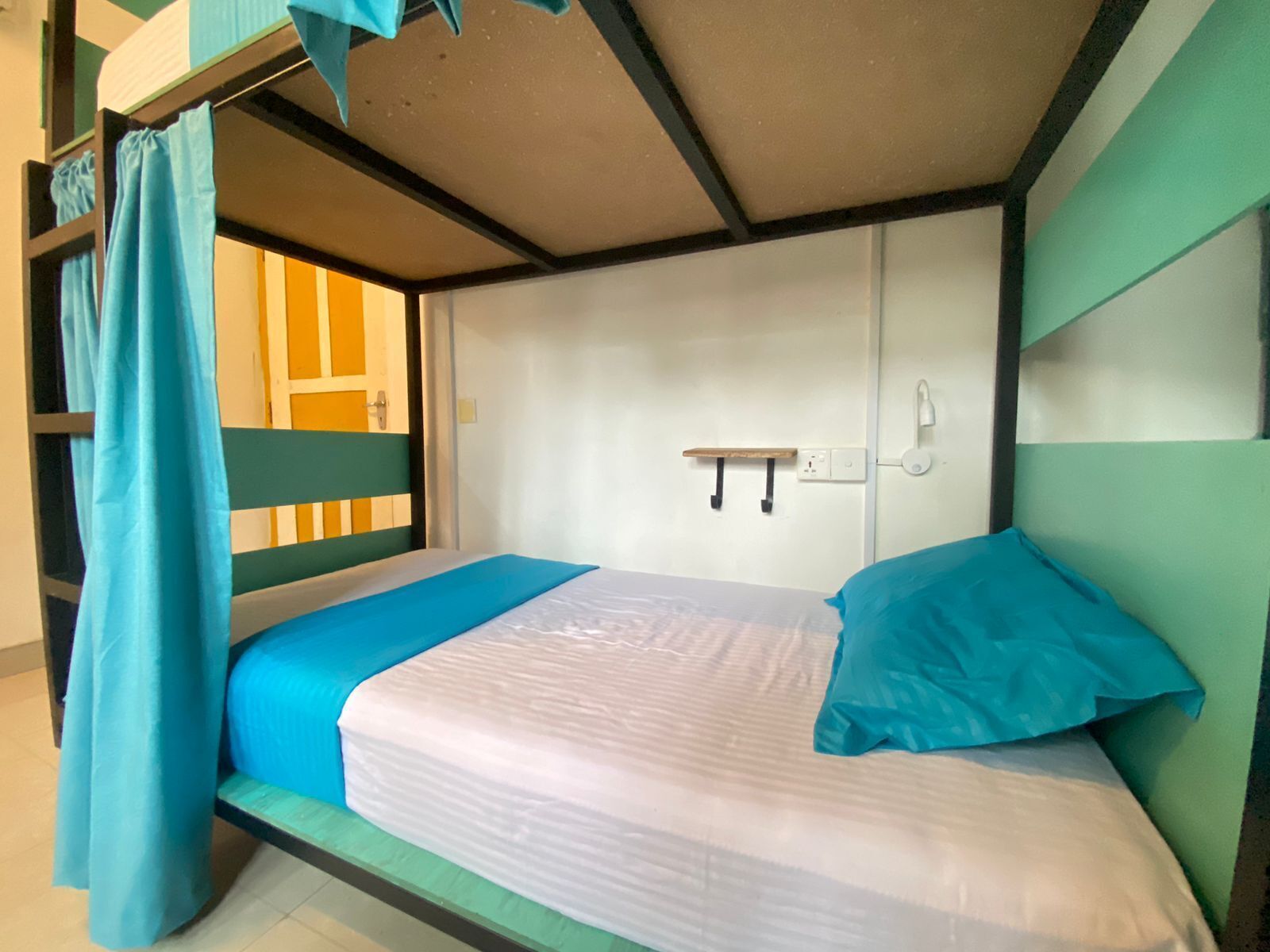 A bunk bed with a blue curtain, a white mattress, and a teal pillow.