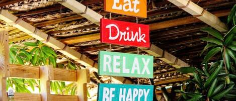 A wooden structure with hanging signs that read "Eat," "Drink," "RELAX," and "BE HAPPY."