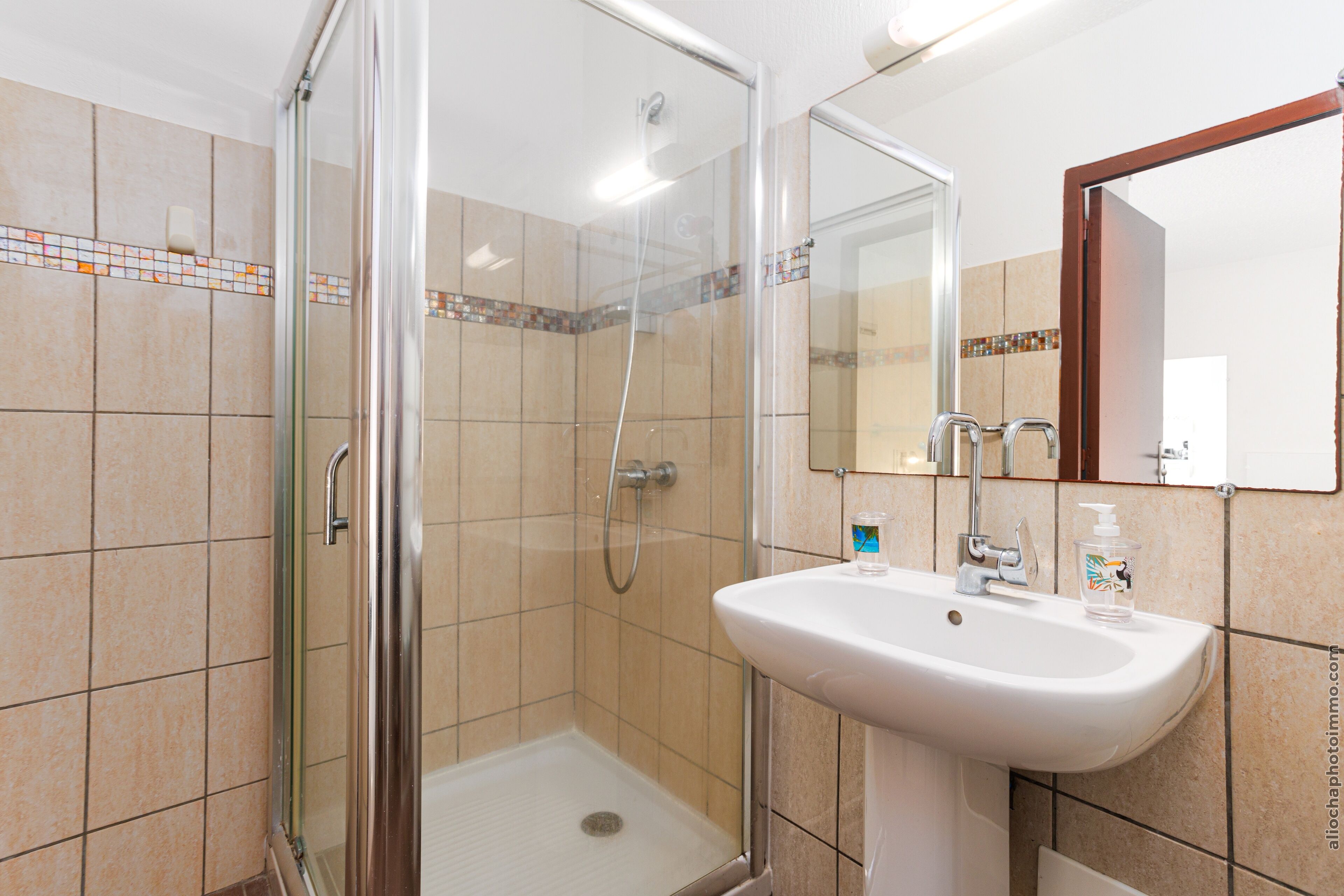 A modern bathroom with a glass-enclosed shower, a white sink, and a mirror with a wooden frame.