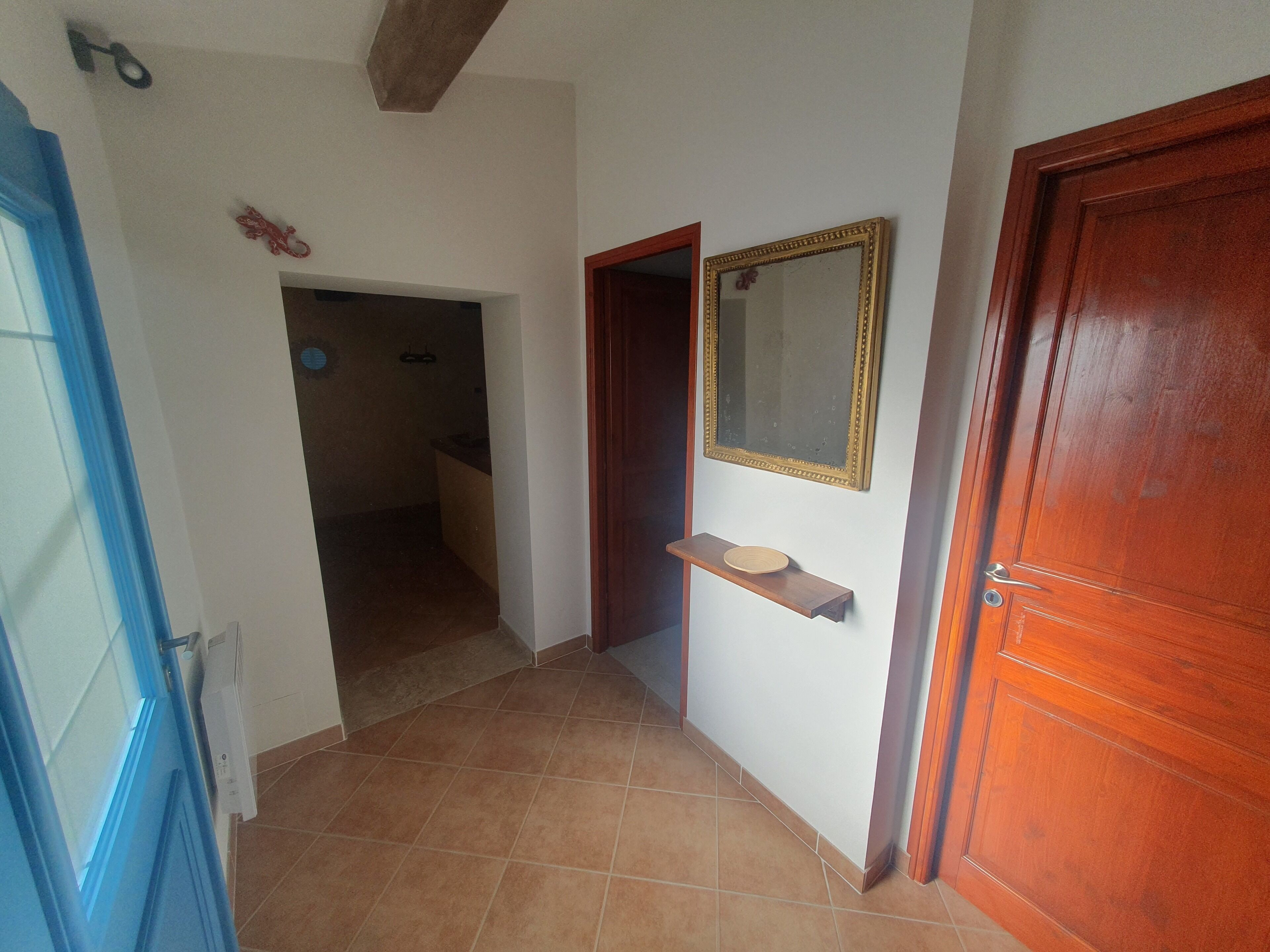 A hallway with a wooden door, a mirror, and a shelf.