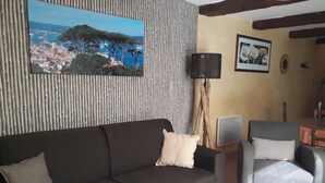 Een woonkamer met een donkerbruine bank, een grijze fauteuil, een lamp en een lijst met een foto van een kustplaatsje.
