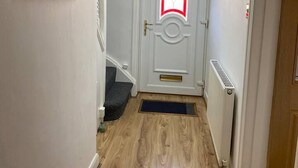 A hallway with a wooden floor, a white door with a red and white design, and a staircase to the left. - The Gold- Home Away From Home (Manchester)