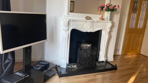 A living room with a fireplace, a television on a stand, and a door with a window. - The Gold- Home Away From Home (Manchester)