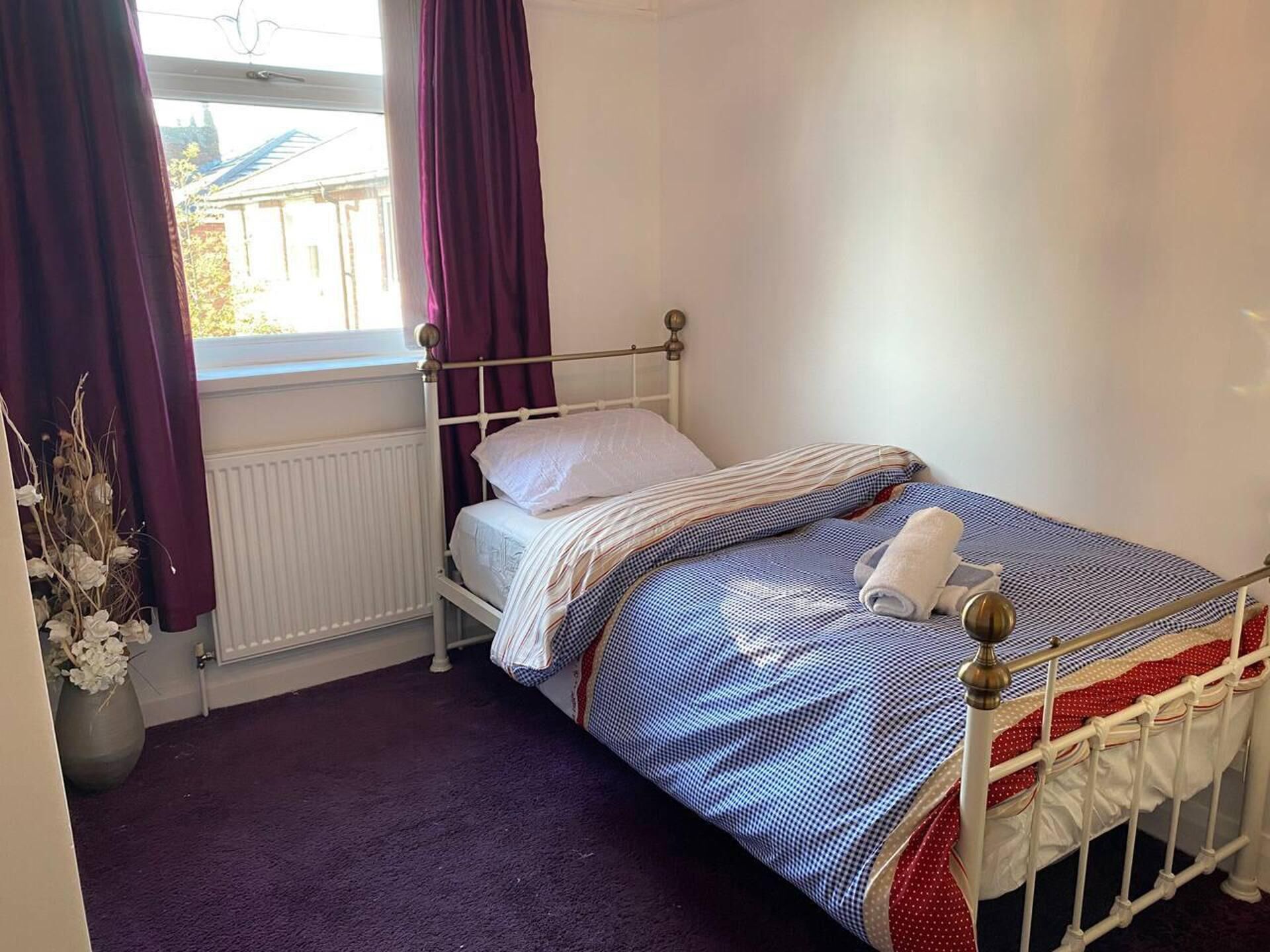 A single bed with a metal frame, white bedding, and a purple carpet.