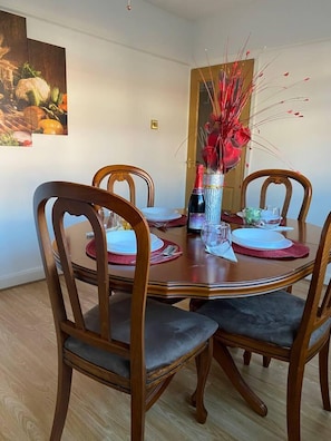 A dining table with four wooden chairs, a vase with red flowers, and a bottle of wine. - The Gold- Home Away From Home (Manchester)
