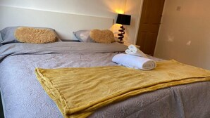 A neatly made bed with a grey patterned duvet, two fluffy pillows, a rolled white towel, and a yellow throw blanket. - The Gold- Home Away From Home (Manchester)
