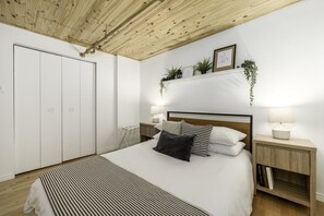 Un dormitorio con cama, mesitas de noche, techo de madera y un armario blanco.