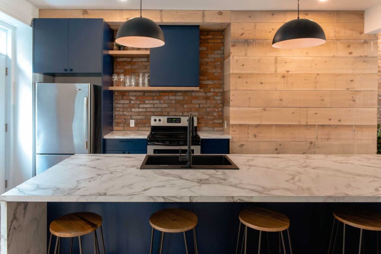 Une cuisine moderne avec un îlot en marbre, des armoires bleues et des éléments décoratifs en bois.