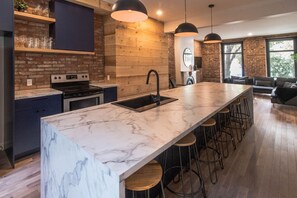 A modern kitchen with a marble island, bar stools, and a brick wall.