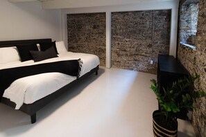 Ein modernes Schlafzimmer mit einem großen Bett, einer Steinwand und einer Topfpflanze.