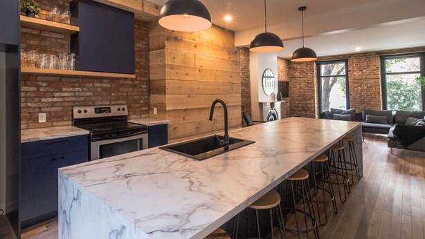 A modern kitchen with a marble island, bar stools, and a brick wall. - Château Deluxe / / Vieux-Québec, Énorme Maison (Québec)