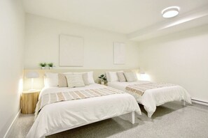 Une chambre avec deux lits, des tables de chevet, des œuvres d’art accrochées au mur et un luminaire au plafond.