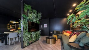 Una sala de estar moderna con piso de madera en espiga, un sofá verde con cojines coloridos, una mesa de centro redonda y un televisor montado en una pared negra con un jardín vertical.