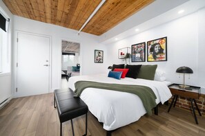 Ein Schlafzimmer mit Holzboden, weißen Wänden, einem Bett mit grüner Decke und einem Nachttisch mit Lampe.