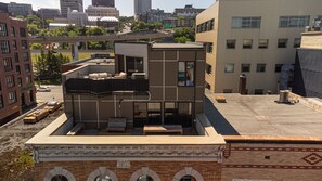 Eine Dachterrasse mit Außenbestuhlung, ein modernes Gebäude mit großen Fenstern und eine Stadtlandschaft im Hintergrund.