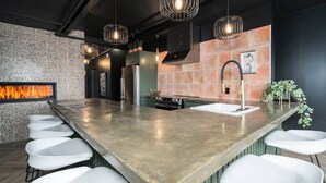 Una cocina moderna con una isla grande, taburetes de bar, horno empotrado e iluminación colgante.