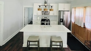 Una cocina moderna con armarios blancos, una isla central con taburetes y una lámpara colgante.