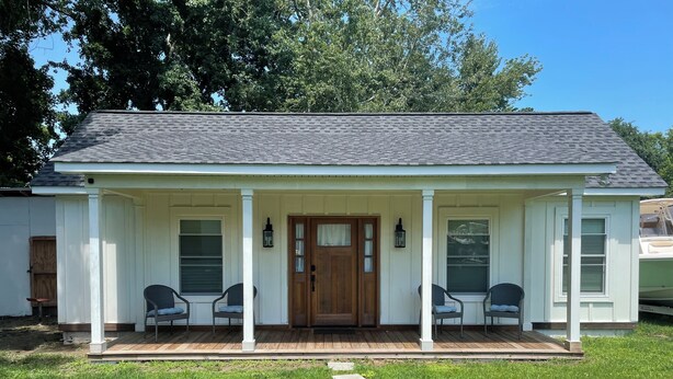 A single-story house with a front porch, two windows on each side, and a wooden door.