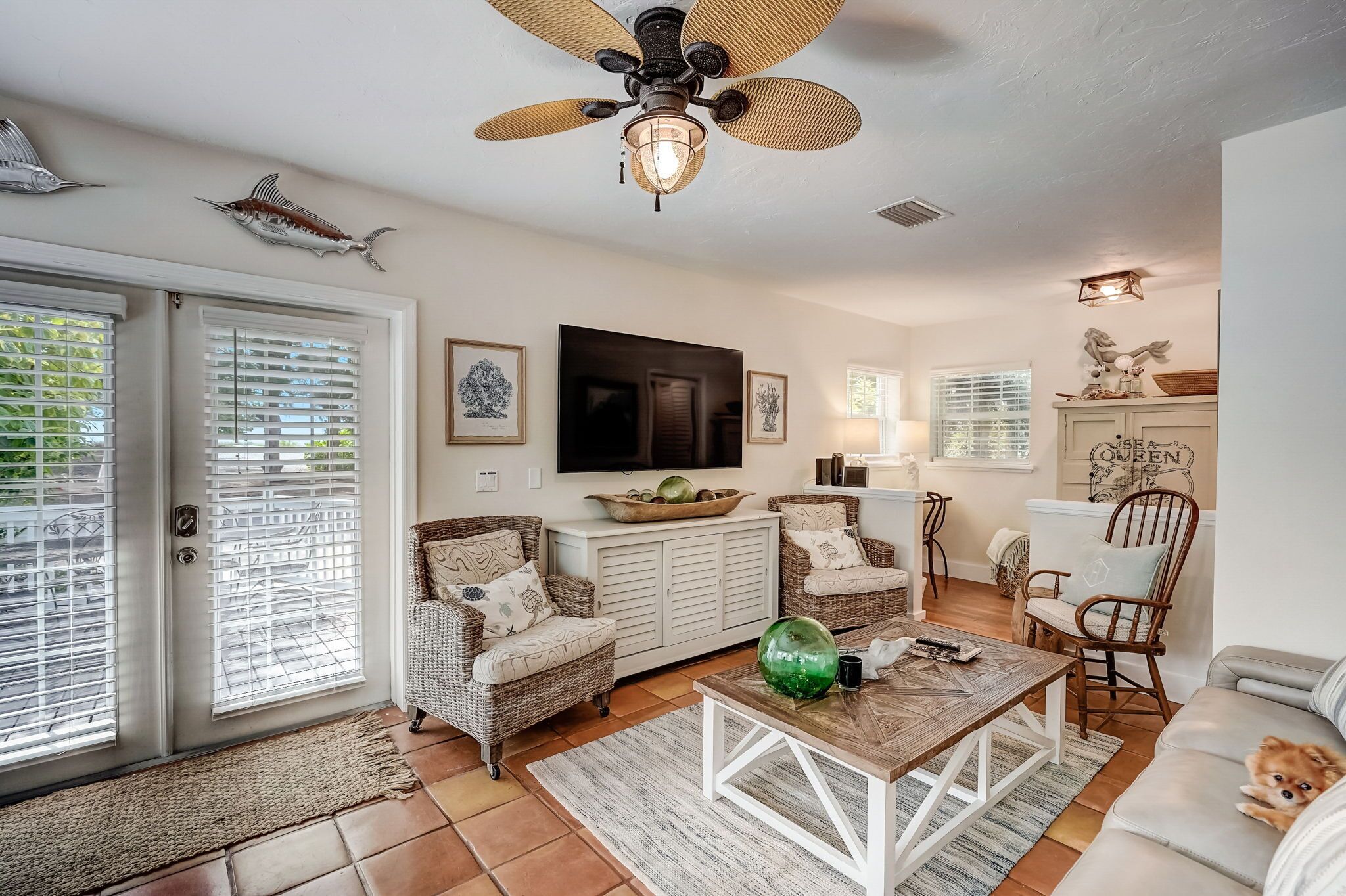 A spacious living room with wicker furniture, a ceiling fan, and a television.