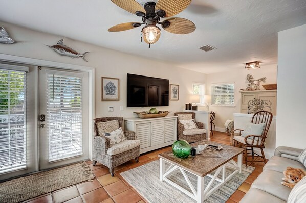 A spacious living room with wicker furniture, a ceiling fan, and a television.