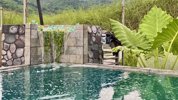 A pool with a stone wall and a waterfall feature, surrounded by lush greenery and mountains in the background. - Jala Jala Casita Blanca Tiny House and Farm Stay with Mountain View and Pool (Jala Jala)