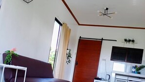 A modern living room with a sofa, a coffee table, a TV, and a kitchen area with cabinets and a countertop. - Jala Jala Casita Blanca Tiny House and Farm Stay with Mountain View and Pool (Jala Jala)