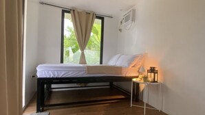 A bedroom with a bed, a ceiling fan, a window with curtains, and a bedside table with a lamp. - Jala Jala Casita Blanca Tiny House and Farm Stay with Mountain View and Pool (Jala Jala)