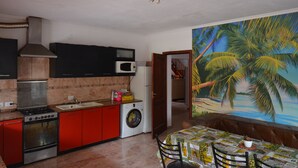 Cucina con mobili rossi, lavatrice e forno a microonde. Sul muro, un murale con palme.