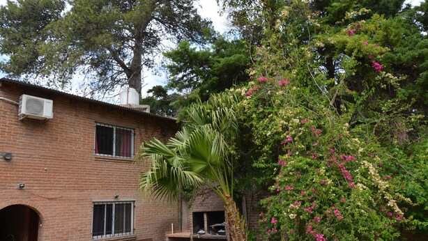 Un edificio in mattoni con un forno a legna, posti a sedere all'aperto e abbondante vegetazione.