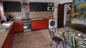 Una cucina compatta con piano cottura, lavello, microonde e lavatrice. È presente un'area pranzo con tavolo e sedie.