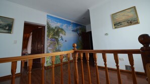 Ein Korridor mit einer Holztreppe, einem Wandgemälde mit tropischer Szenerie und einem gerahmten Gemälde an der Wand.