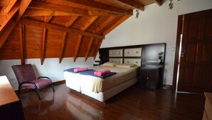 Ein Schlafzimmer mit Holzboden, einem Bett, einem Sessel, einem Nachttisch und einer Tür.