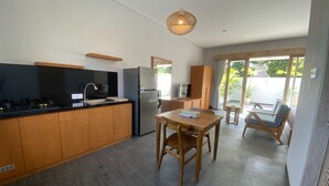 Et moderne køkken med træskabe, en sort bordplade og et indbygget komfur. Der er et spiseområde med et bord og stole, og et stort vindue giver naturligt lys.