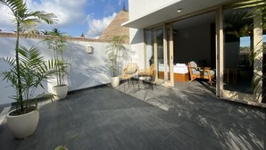 En moderne udendørs terrasse med en stråtækt konstruktion, plantekasser og et siddeområde med en seng.