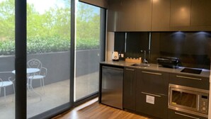 A modern kitchen with dark cabinetry, a built-in oven, and a large window overlooking a balcony with outdoor furniture.