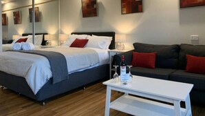A modern hotel room with a bed, a sofa, a coffee table, and artwork on the walls.