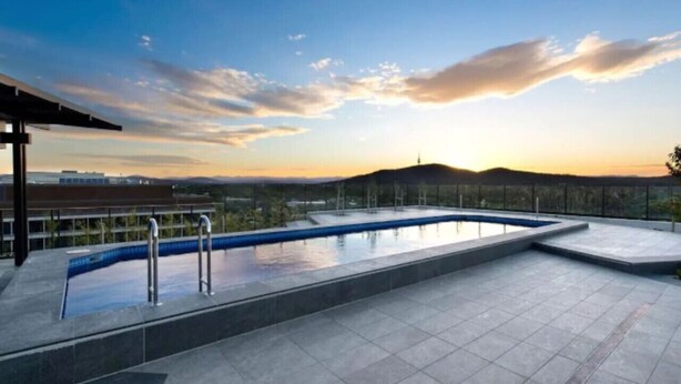 A rooftop pool with a view of the sunset and distant hills.